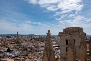 It is silent up here, the sounds of the streets seem far away. All you hear are the cries of seagulls and the wind tearing around lime stone pillars and arches. It is not only the vistas that are breathtaking but the unique sensation of being at the place where sky meets heaven. From the roof terraces of La Seu, Mallorca's cathedral, Palma looks like a colorful patchwork rug lined with a wide stripe of blue. In awe you stroll under the flying buttresses, the characteristic stone arches. They used to be out of reach, now you can respectfully touch them. See up close how the humid, salty air damages the soft stone. And detect the work of the masons who have mended and repaired over the centuries, and still do. My favorite elements are the fierce gargoyles, watching grimly from above as if to attack any minute. The waterspouts are often imaginary beasts, meant to protect the cathedral and the people of Palma. On the east terrace you meet La Seu’s famous rose window at eye level. With more than 11 meters in diameter the Gothic Eye is one of the largest worldwide, its over one thousand original glass elements priceless. Twice a year, on February 2 and November 11, the rose window aligns with the sun for a spectacular light show. Called El Espectáculo del Ocho because of the colorful 8 that appears on the opposite wall above the entrance. The way to the rooftop leads along a narrow spiral staircase of 215 steps. You pass historic graffiti of early refugees and tiny lookouts that allow first vistas from within. In the bell tower you get a glimpse of Eloi. The largest of the cathedral’s nine bells is the only one still rung by man. Actually you need nine to eleven men to move its 4.500 kg. Because the wooden structure of the bell tower is endangered by the momentum Eloi only rings on rare occasions. When the pope or bishop died, when a new pope was elected, and once a year on Corpus Christi. For centuries the roof terraces of La Seu have been unaccessible, dark, insecure and littered. Just a few years ago they were cleaned up and opened to the public. From May till October you can register online now for a guided one-hour-tour. Allowing a fabulous overview of La Seu’s eventful history and architecture as well as Palma’s vibrant presence